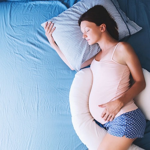 a pregnant woman sleeps with a j-shape pillow