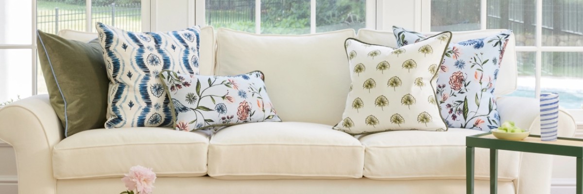 olive, white and navy pillows and bolsters on a light beige sofa